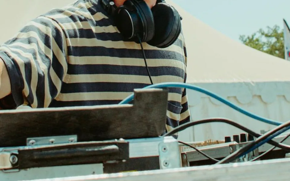 Jeune DJ mixant sous un chapiteau blanc en extérieur, en journée