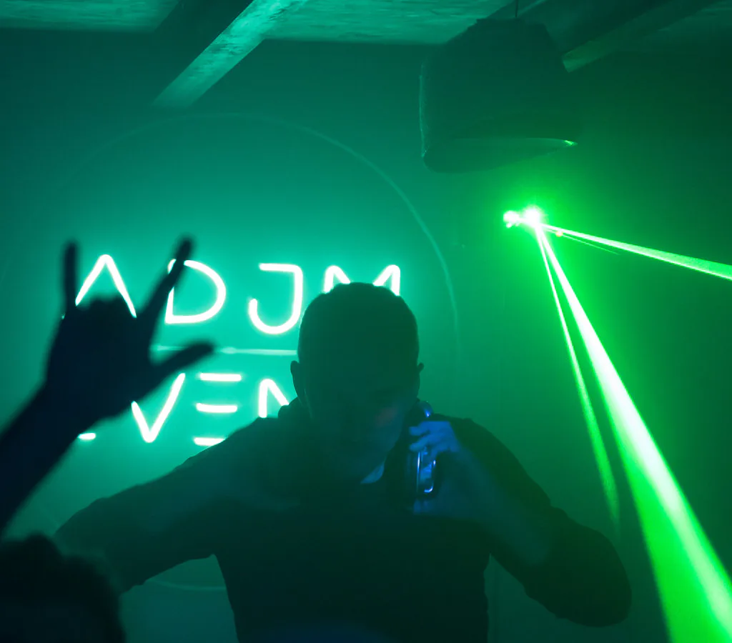 Régie DJ et laser vert pendant une soirée, logo ADJM en arrière-plan