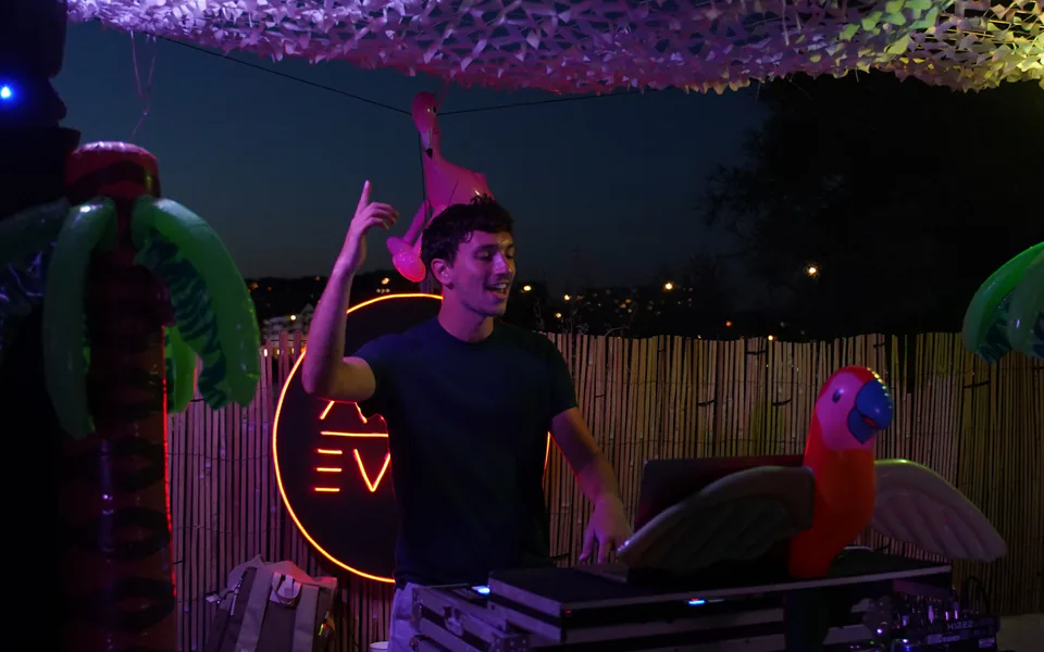 DJ aux platines en extérieur, de nuit, devant un néon ADJM Event